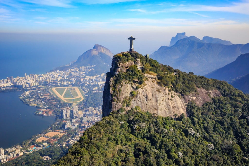 Statue of Christ the Redeemer on a mountain peak with city and ocean view
