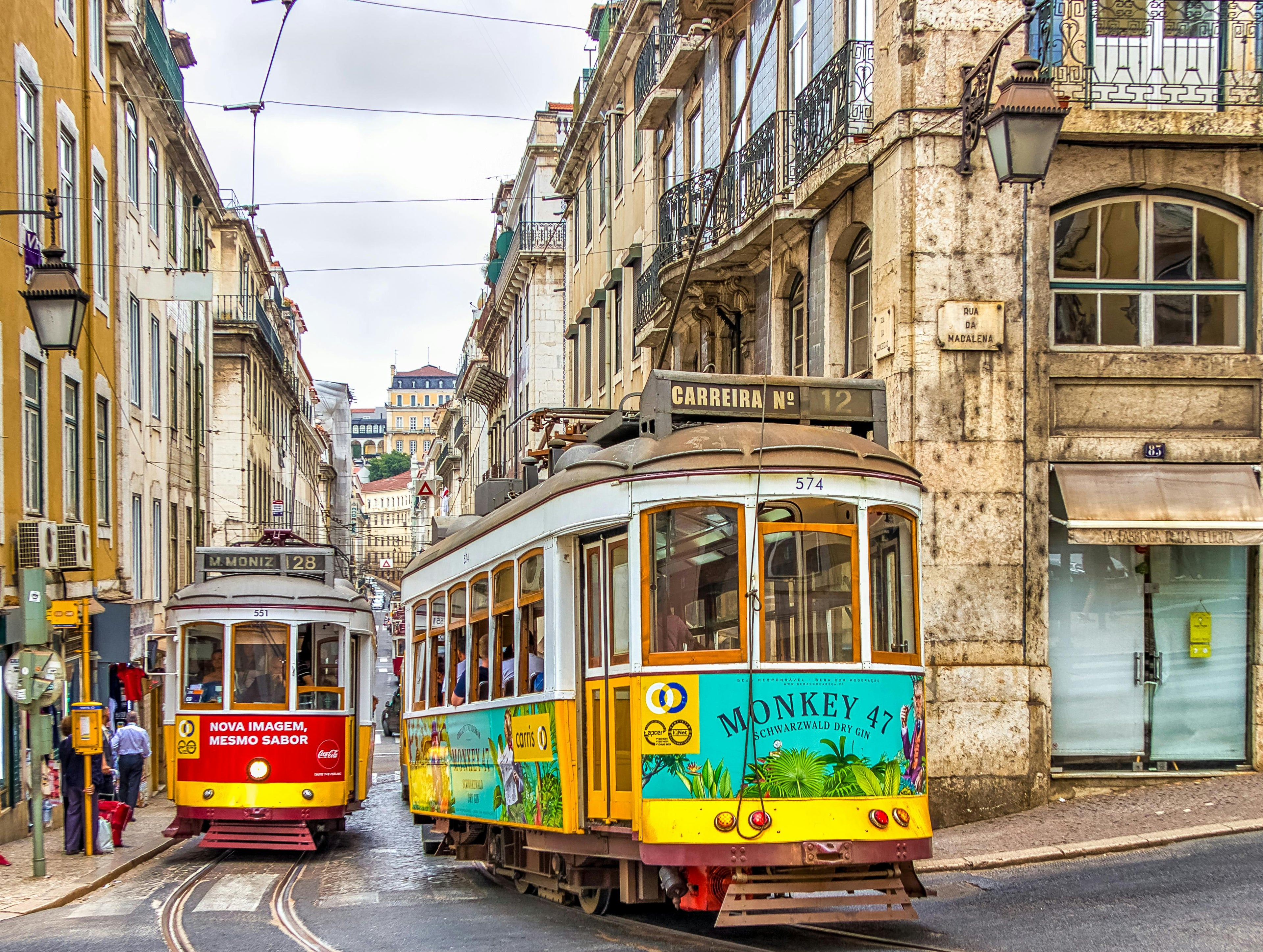 Two trams on a city street with colorful designs and architectural buildings in the background.