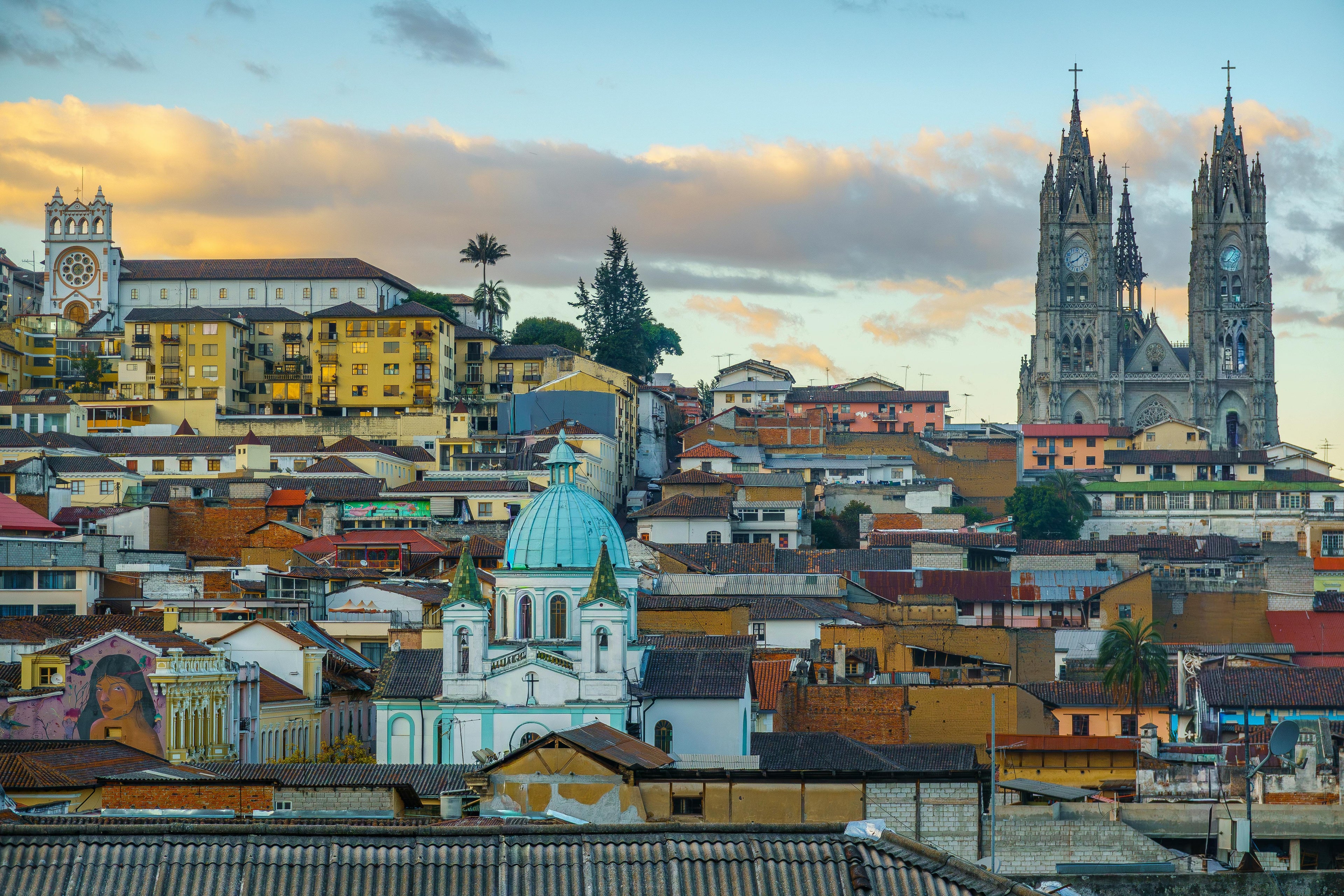 Cityscape with a prominent cathedral and colorful buildings under a sunset sky.